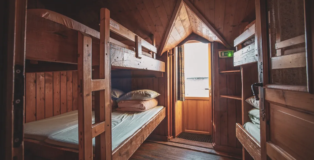 Chambre en bois douillette avec lits superposés, baignée de lumière et vue sur les montagnes.