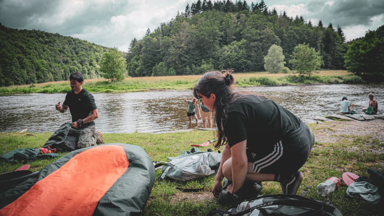 Deelnemers bereiden hun packrafts voor aan de oever van een rivier omringd door weelderig groen.