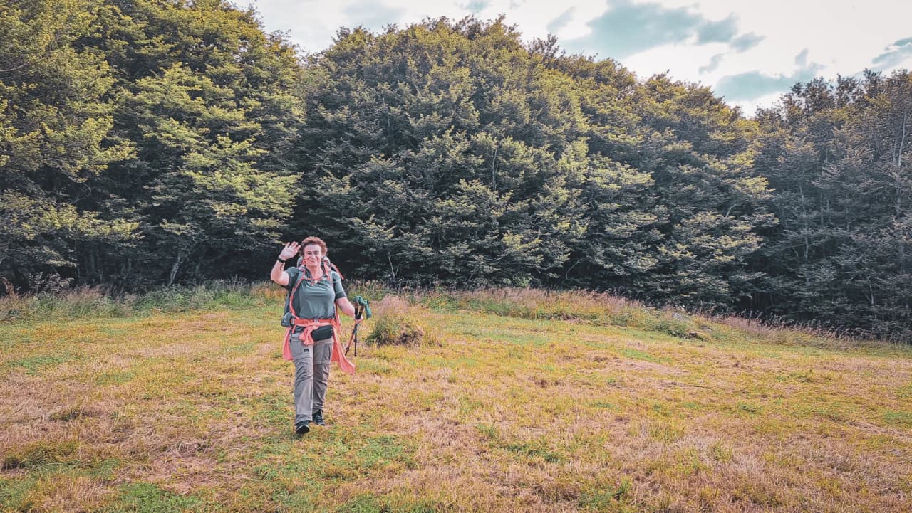 Une randonneuse souriante sur un sentier verdoyant des Vosges, entourée de nature luxuriante.