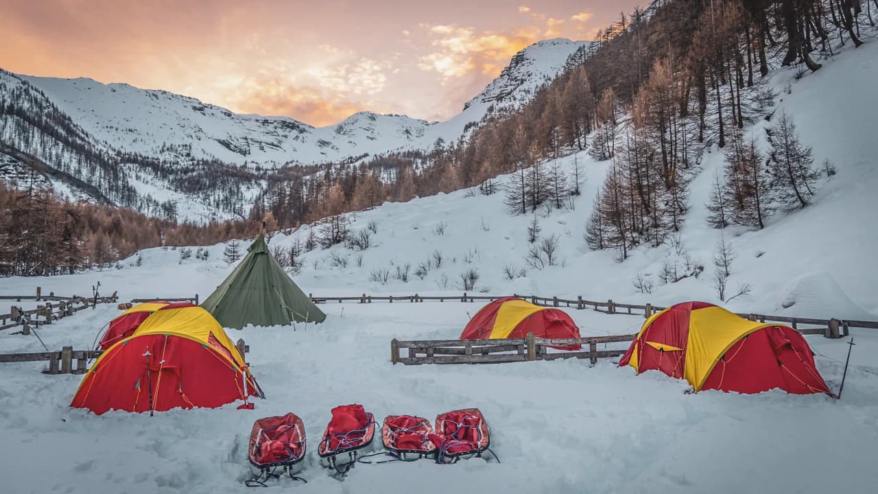 Kleurrijke tenten in een besneeuwd landschap van het Écrins-gebergte, met majestueuze bergen bij zonsondergang.