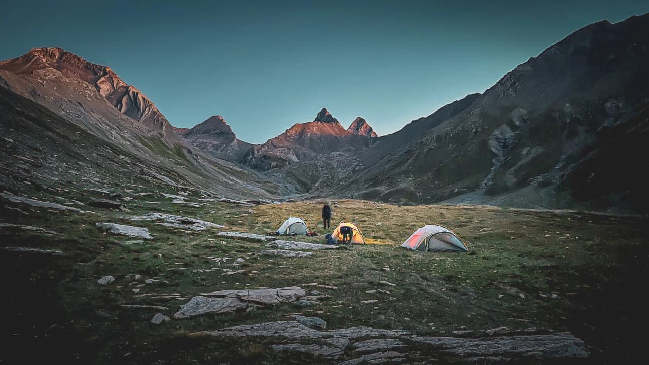Bivouac alpin sous les Aiguilles d'Arves, tentes illuminées au crépuscule, panorama majestueux.