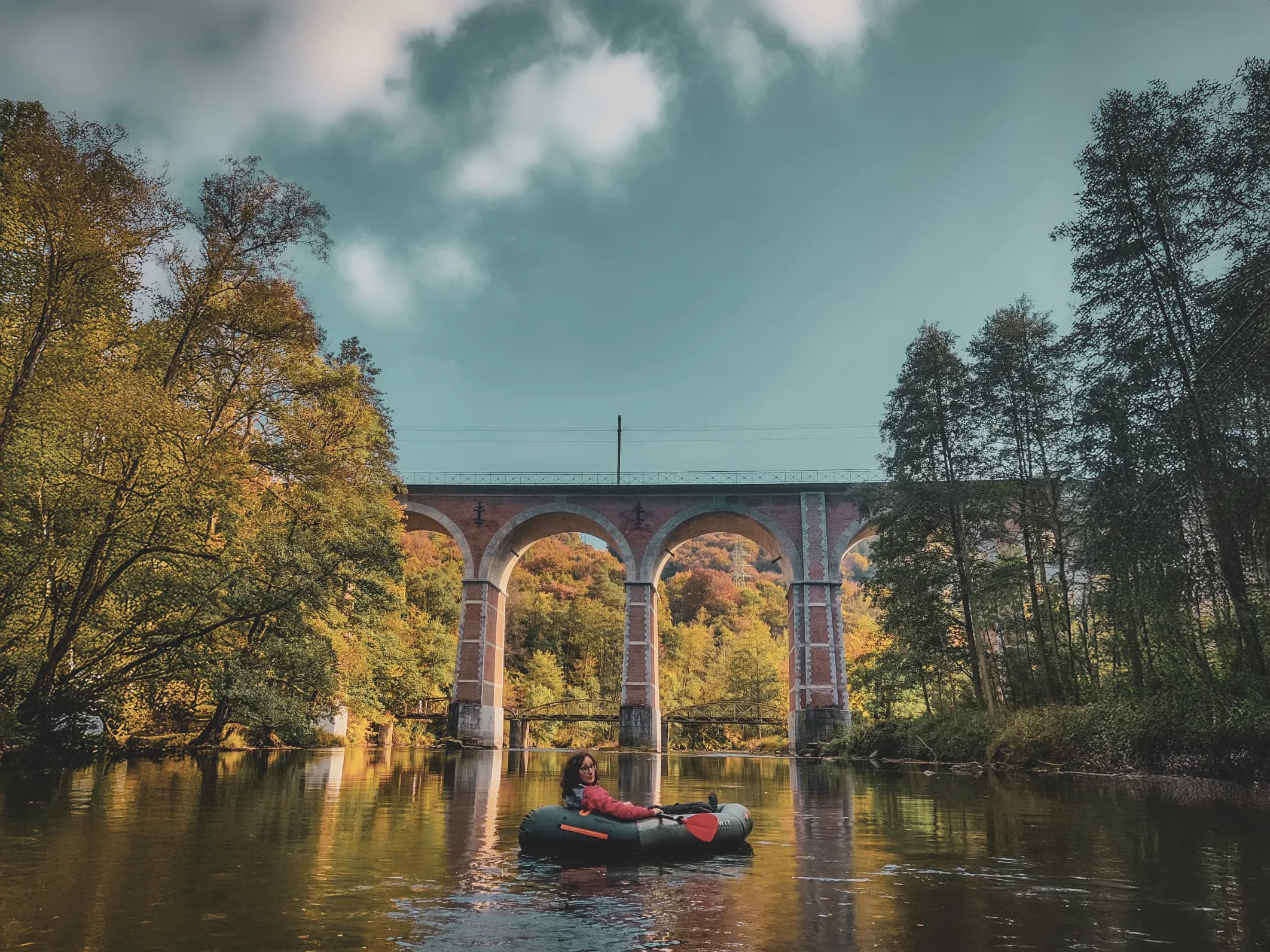 Packraft expedition on a river surrounded by autumn landscapes and a majestic viaduct.