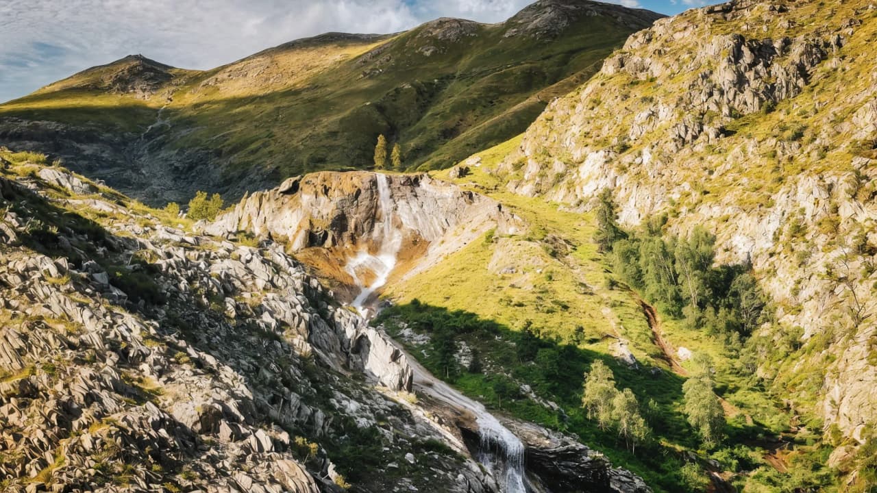 Paysage de montagne majestueux avec chutes d'eau, verdure luxuriante et rochers sculptés par la nature.