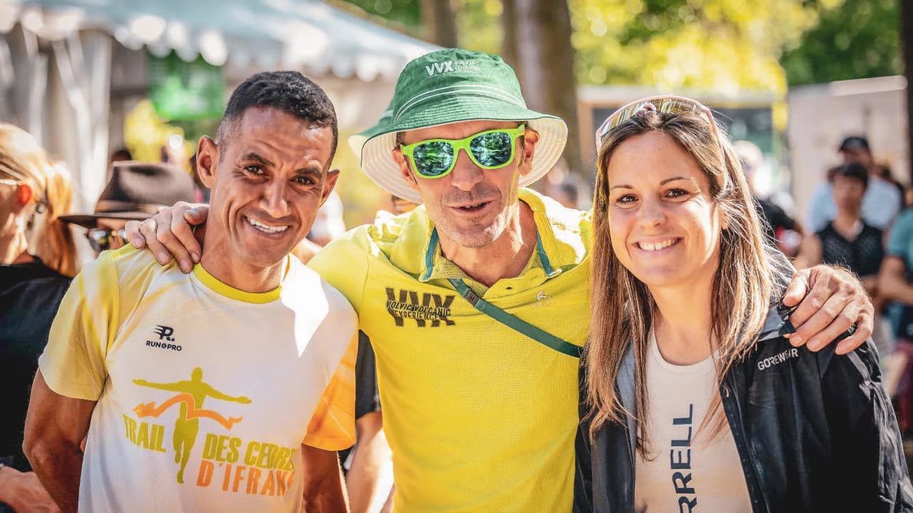Three smiling athletes pose together in a sunny setting, surrounded by nature.