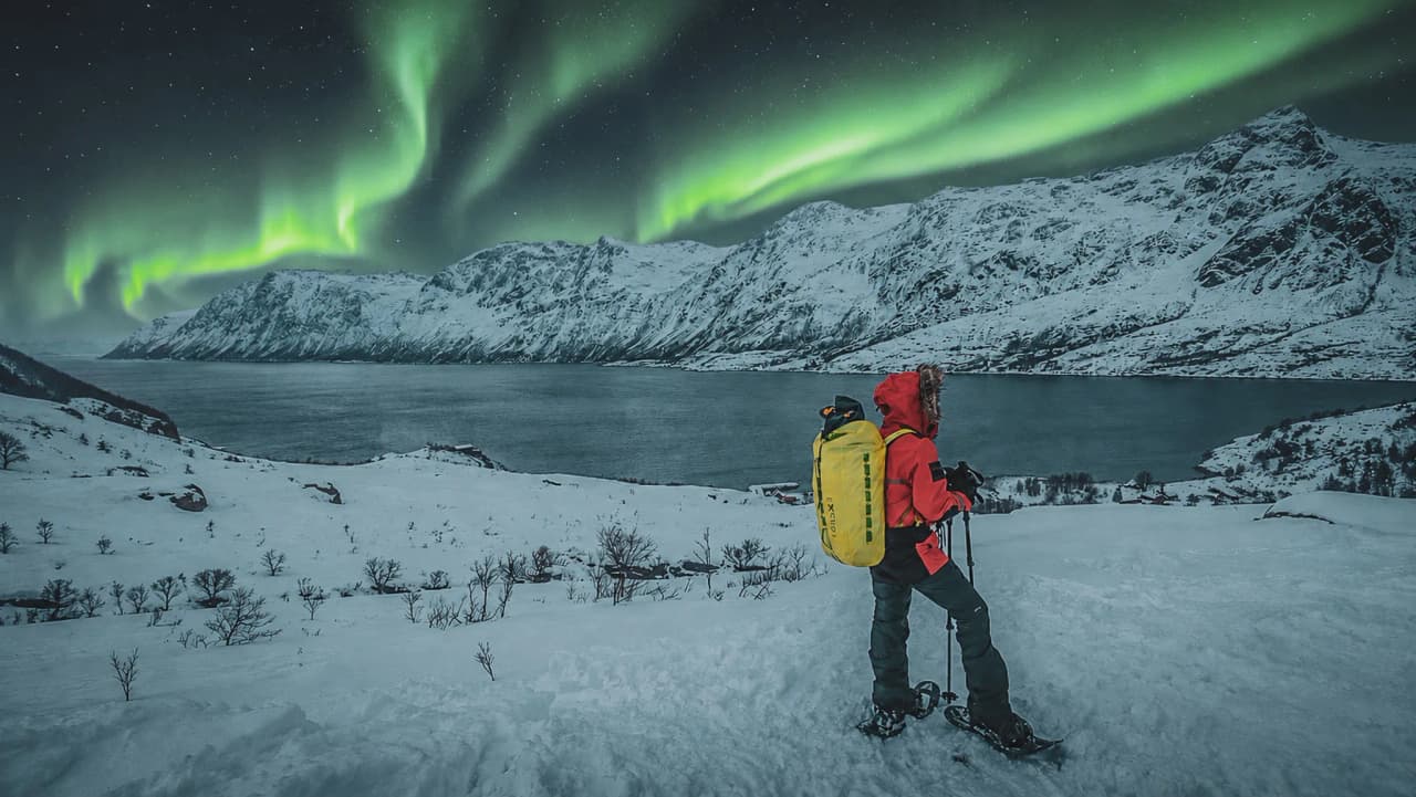 Een avonturier op sneeuwschoenen bewondert het noorderlicht boven een besneeuwd landschap in Tromsø.