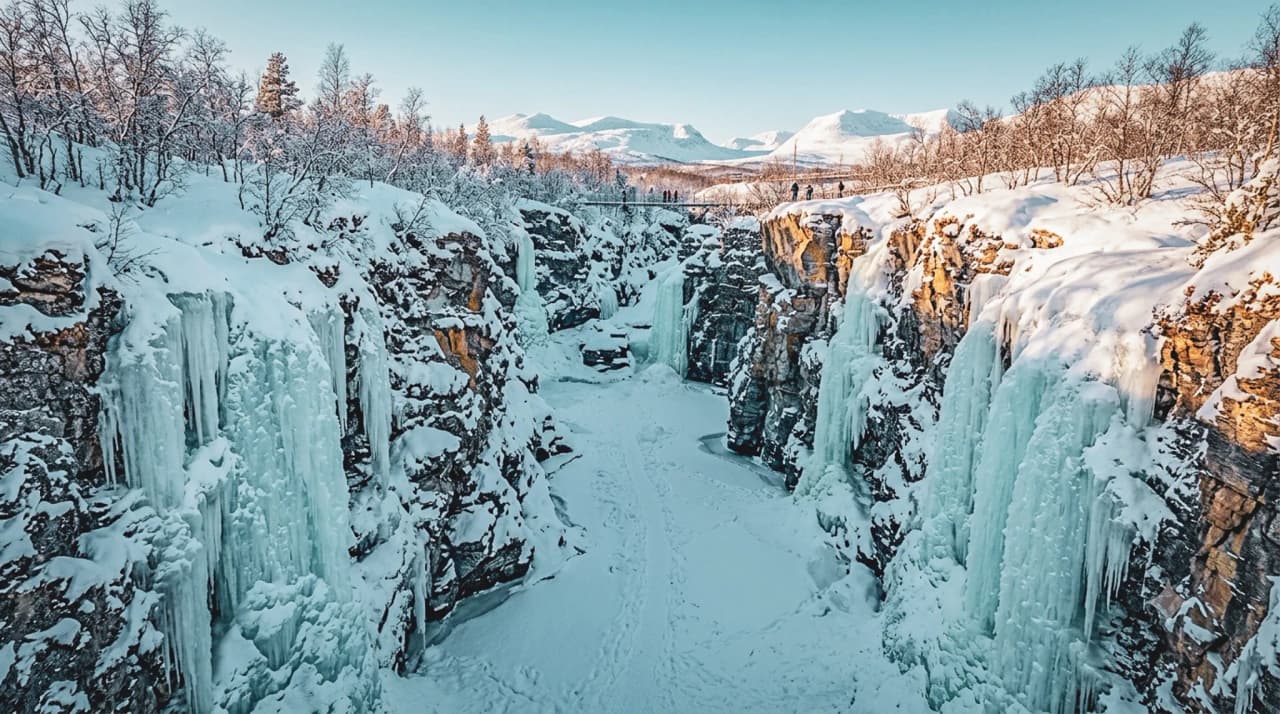 Een bevroren kloof in Lapland, omgeven door stralende sneeuw en majestueuze rotswanden.