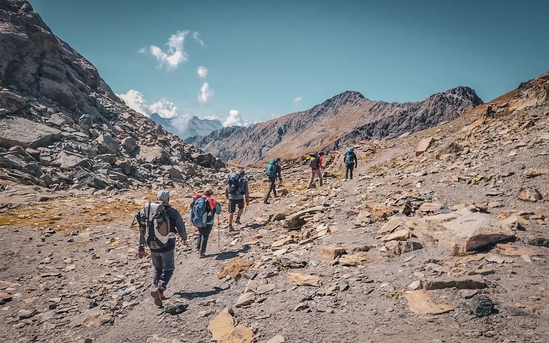A group of hikers on a mountain trail under a blue sky, surrounded by spectacular scenery.