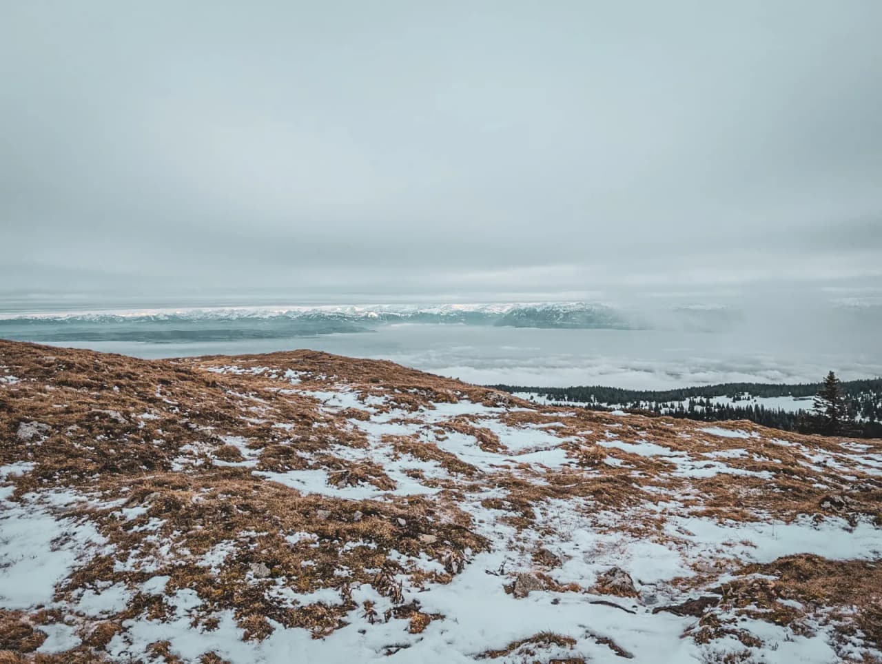 Paysage hivernal du Jura suisse, avec des montagnes enneigées sous un ciel nuageux.