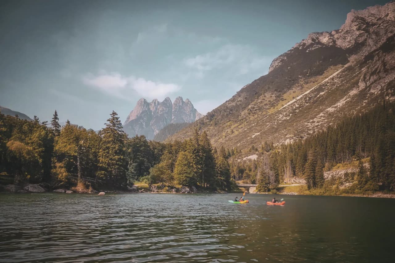 Two packrafts sail peacefully on an alpine lake, surrounded by majestic mountains and lush green forests.