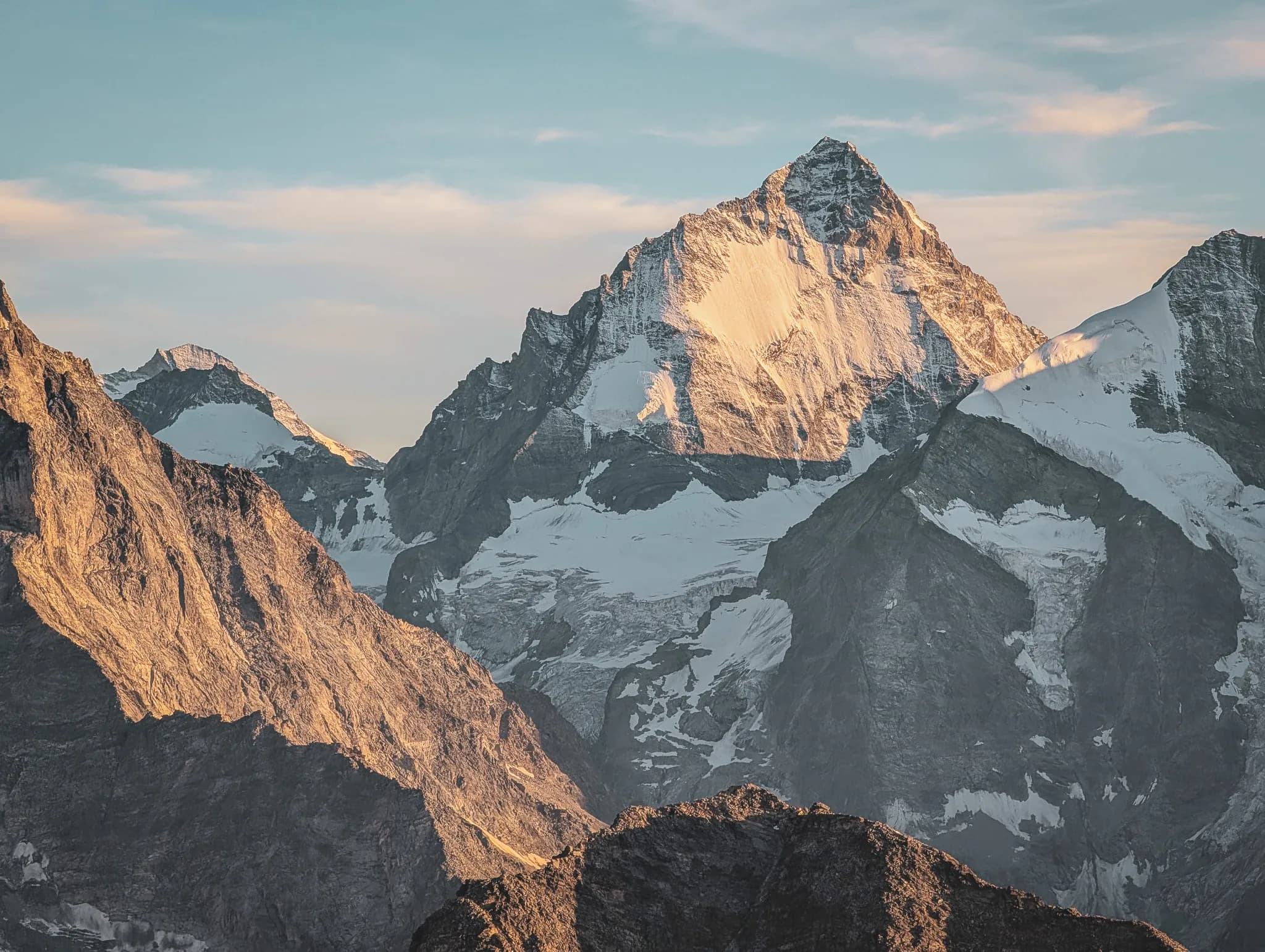 A modern, angular building sits on a mountain ridge, surrounded by craggy rocky landscapes and majestic peaks.