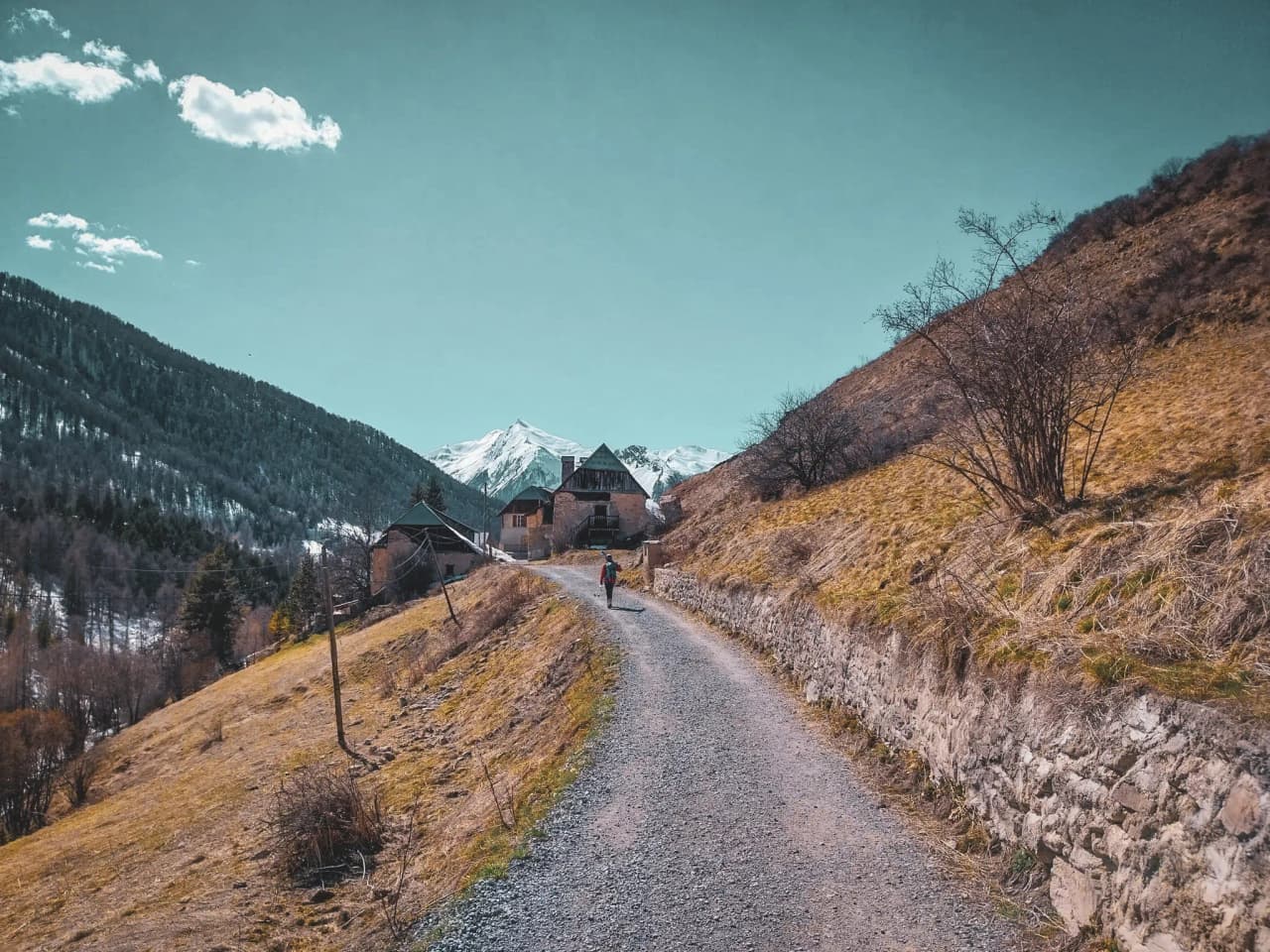 A winding path leading to a mountain village, with majestic mountains in the background.