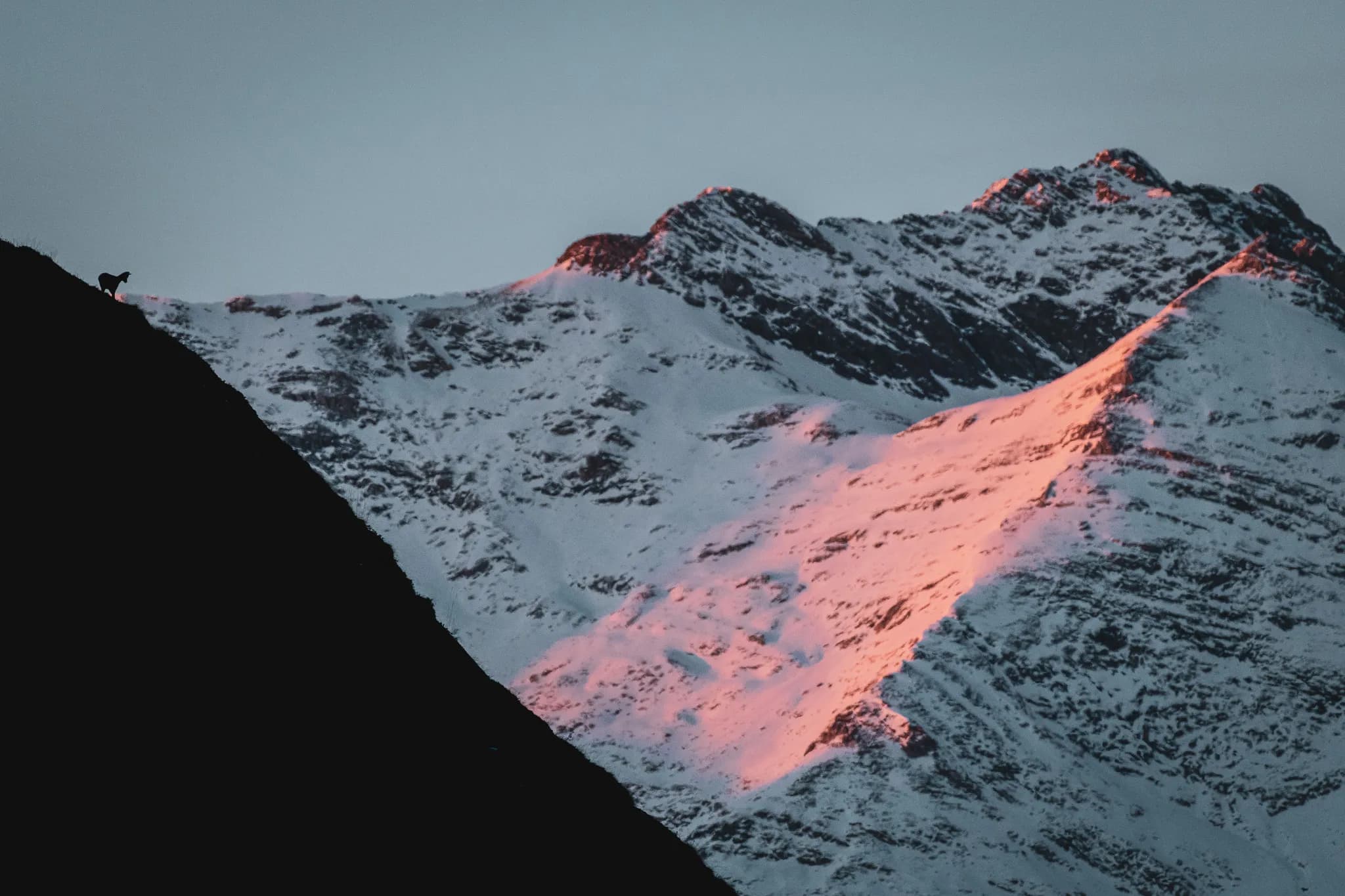 A majestic landscape in the Pyrenees, with snow-capped mountains illuminated by the sunset.