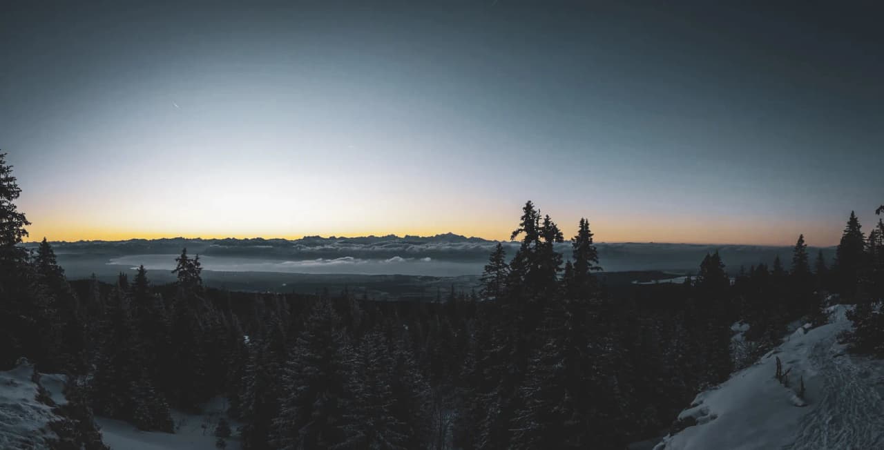 Panorama enneigé du Jura, forêts majestueuses et montagnes au crépuscule invitant à l'aventure.