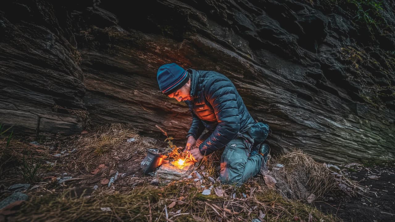 An adventurer lights a fire in the heart of the Vercors forests, surrounded by wilderness.
