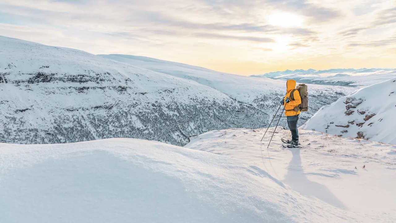 Een sneeuwschoenwandelaar bewondert het besneeuwde landschap van Noors Lapland bij zonsondergang.