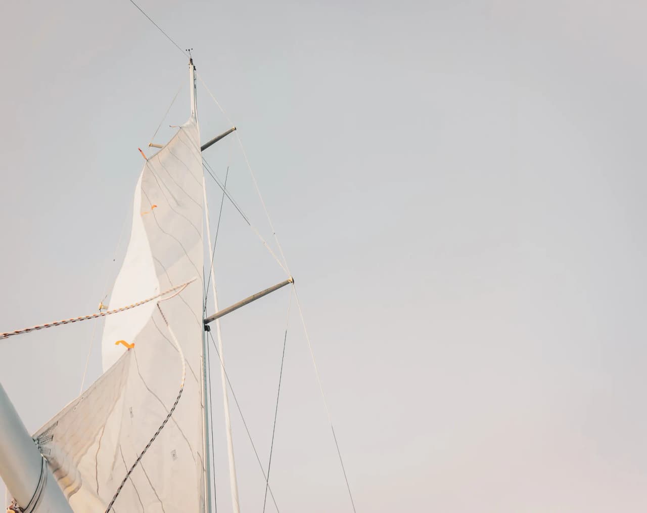 Voile blanche d'un bateau s'élevant vers un ciel lumineux, invitant à l'aventure maritime.