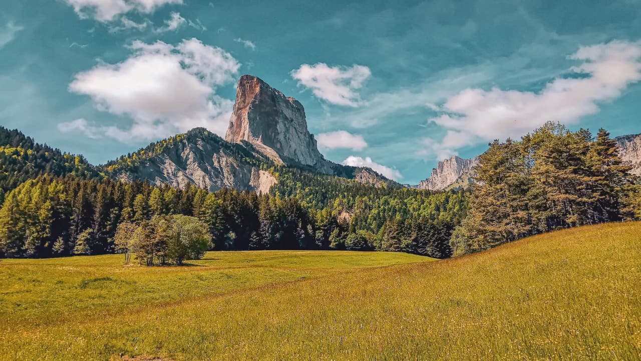 Majestic Mont Aiguille overlooking lush green meadows, blue skies and soft clouds.