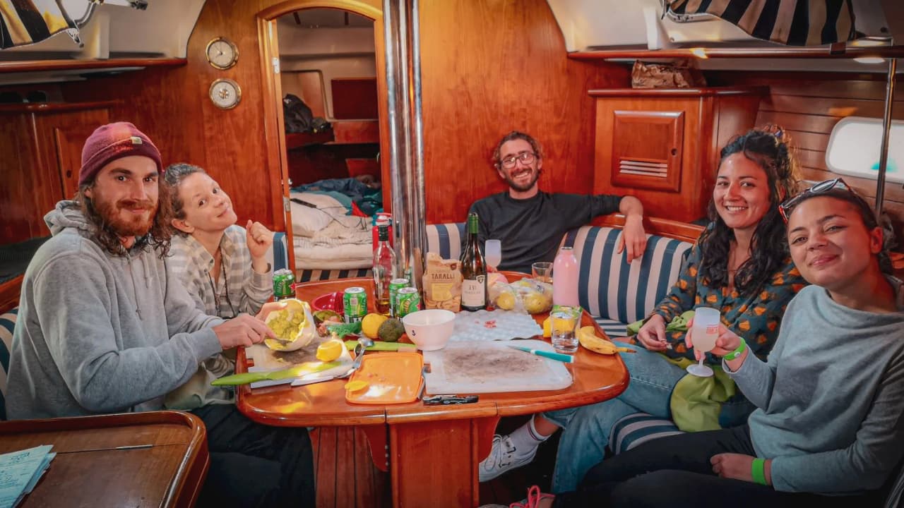 Een groep gelukkige vrienden rond een tafel op een zeilboot, samen eten en lachen.