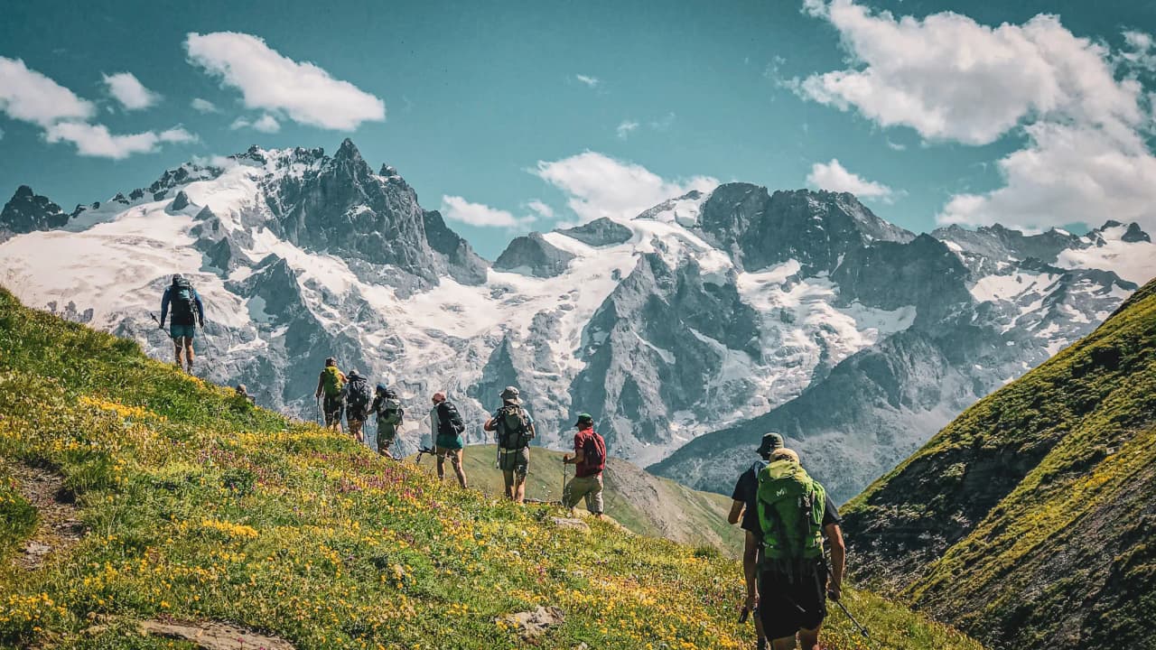 Un groupe de randonneurs sur un sentier alpin, face aux majestueux sommets enneigés.