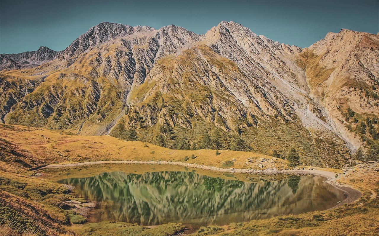 A peaceful lake reflecting majestic mountains under a sunny sky in the Queyras.