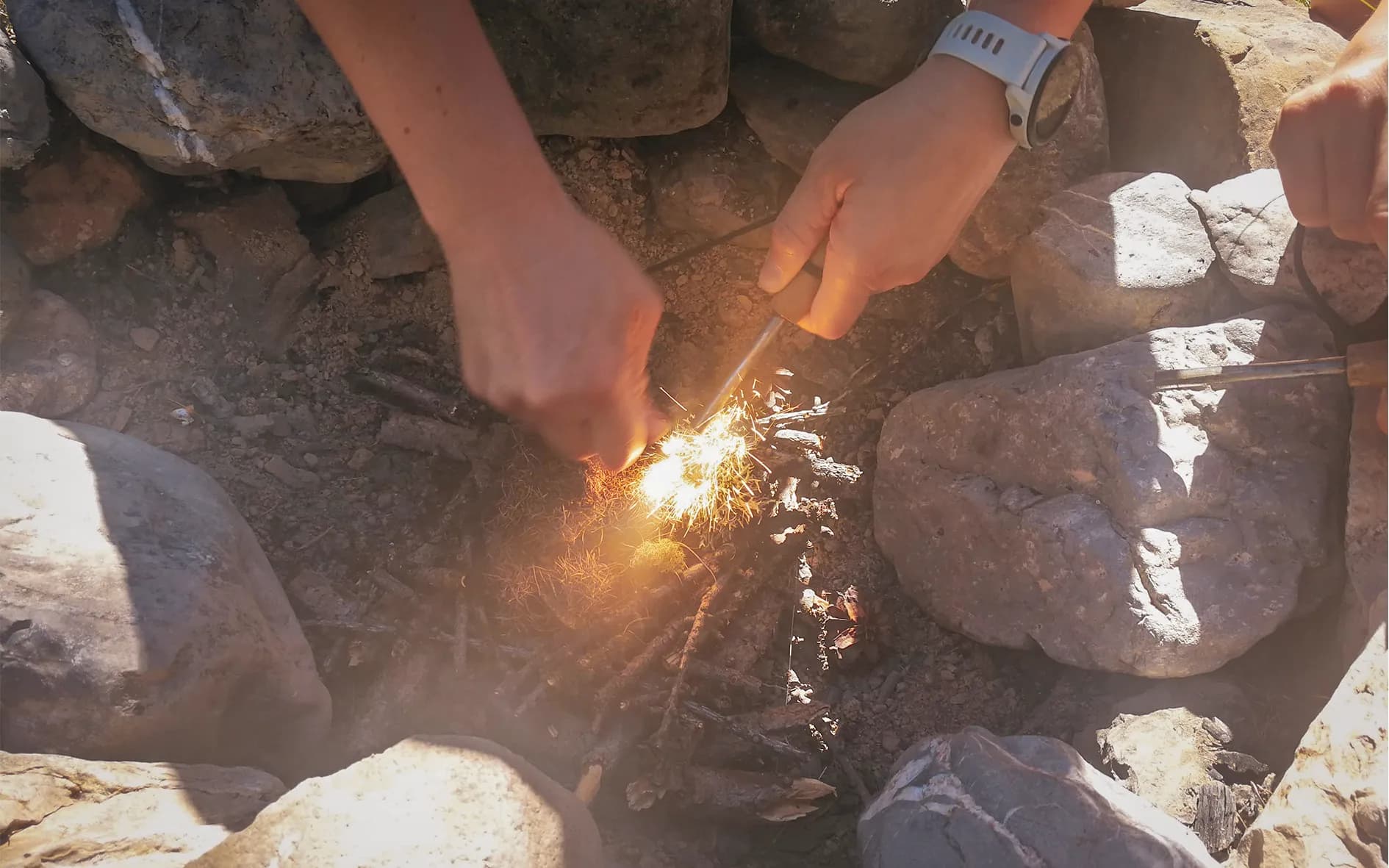 Hands lighting a fire with sparks, surrounded by rocks, in the heart of nature.