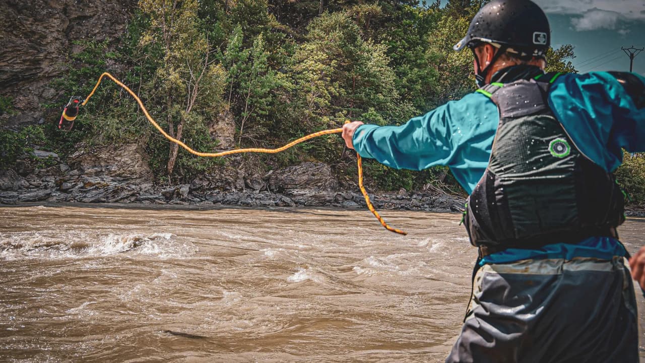 Een man in packraft-uitrusting die een touw in een door groen omgeven rivier gooit: avontuur gegarandeerd!