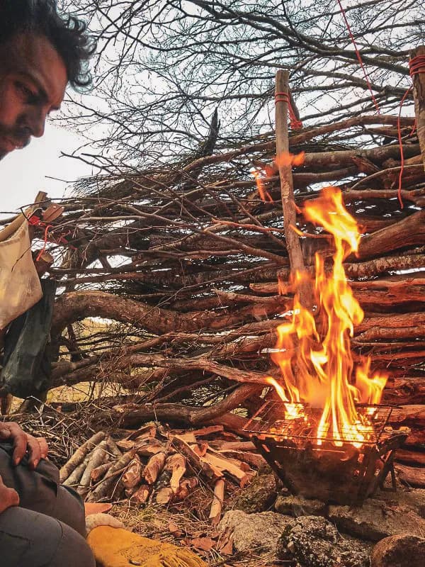 Een knapperend vuur voor een houten schuilplaats in het wild, een meeslepende bushcraftscène.