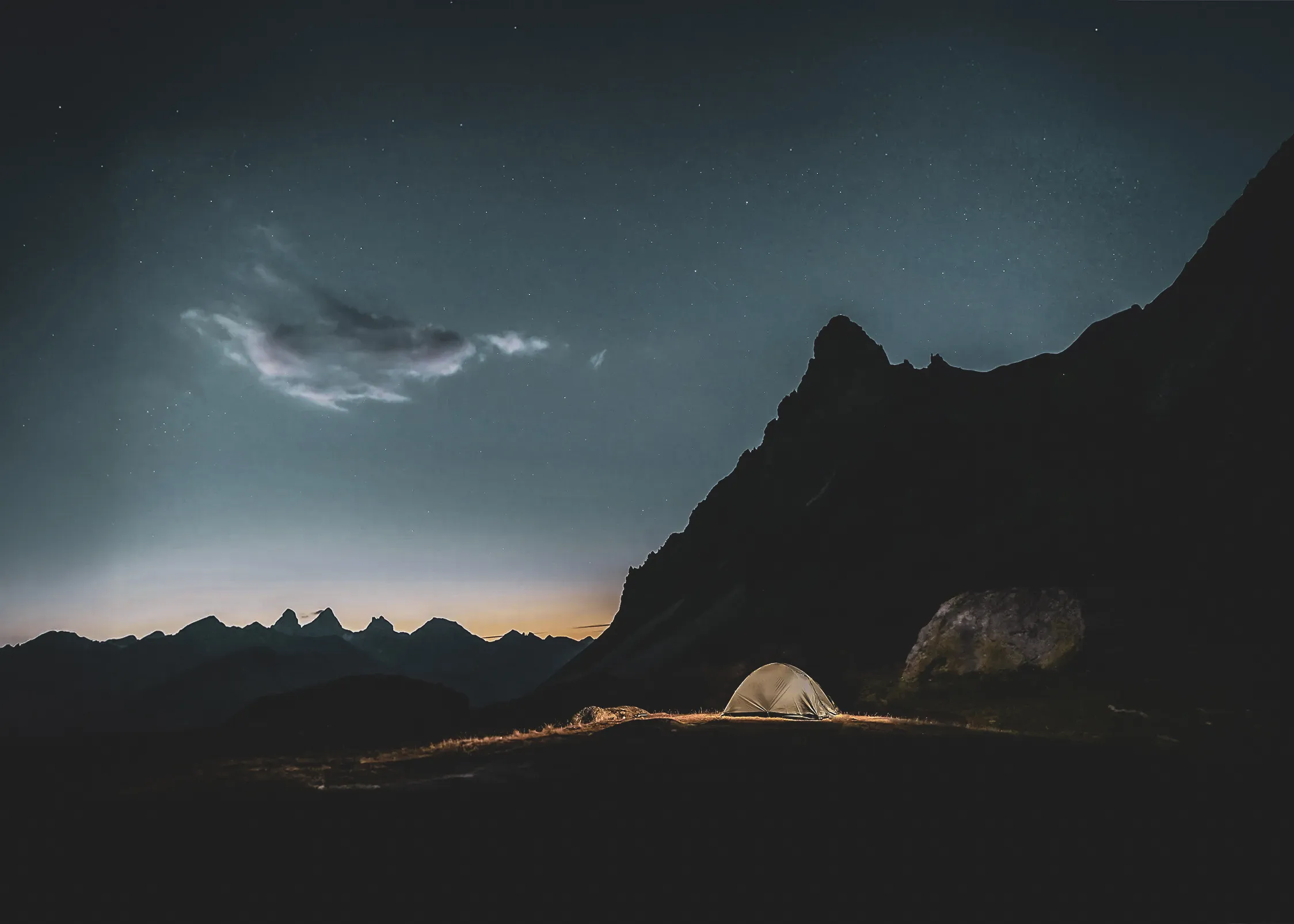 Tente éclairée sous un ciel étoilé, entourée de majestueuses montagnes nocturnes.