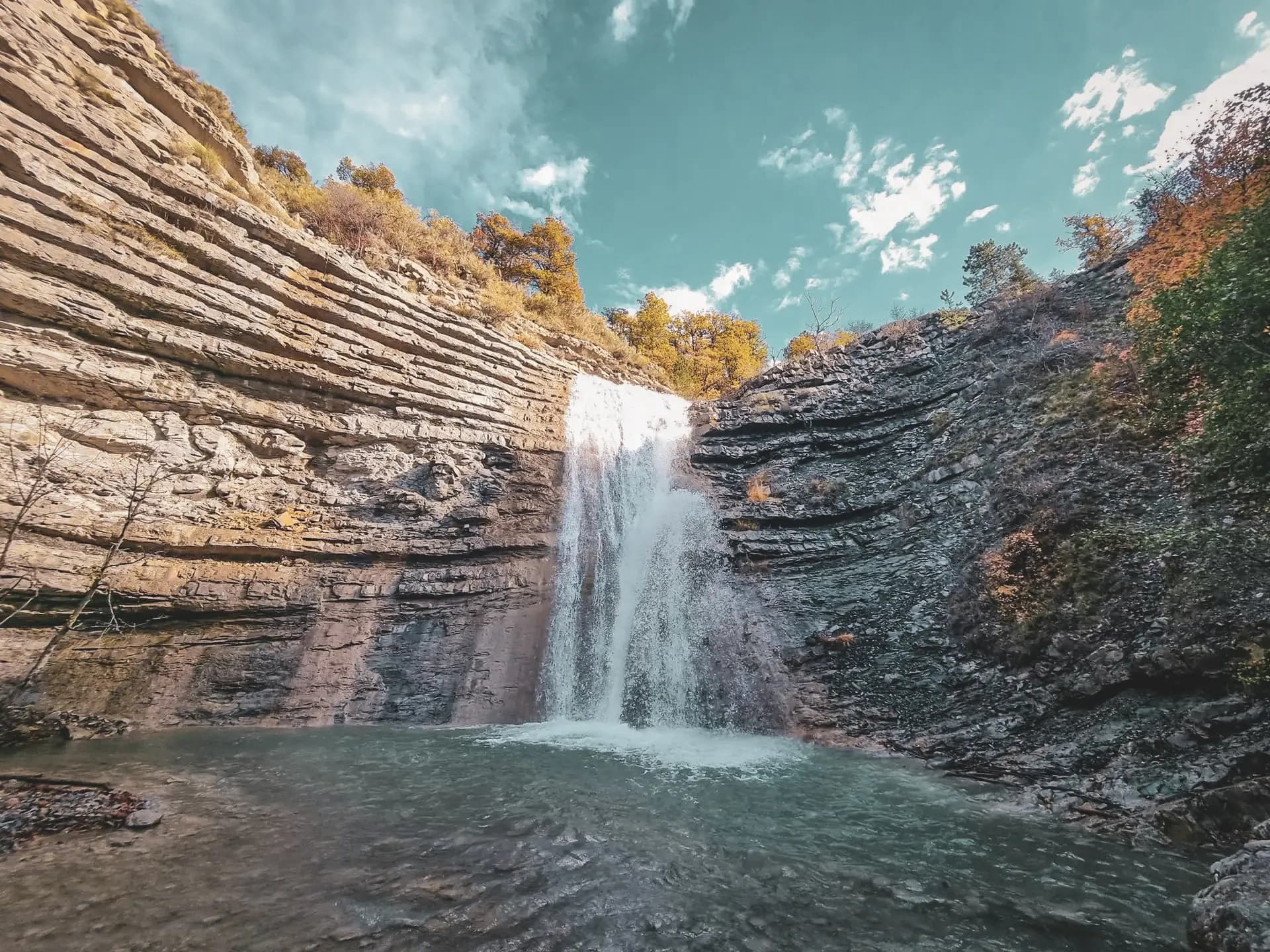 Cascade majestueuse entourée de falaises stratifiées et d'une eau cristalline, invitation à l'évasion.