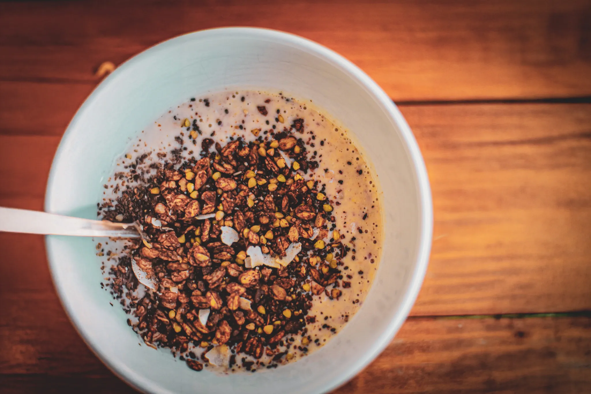 Bowl of crunchy granola with milk, on a wooden table, perfect for breakfast at a yoga retreat.