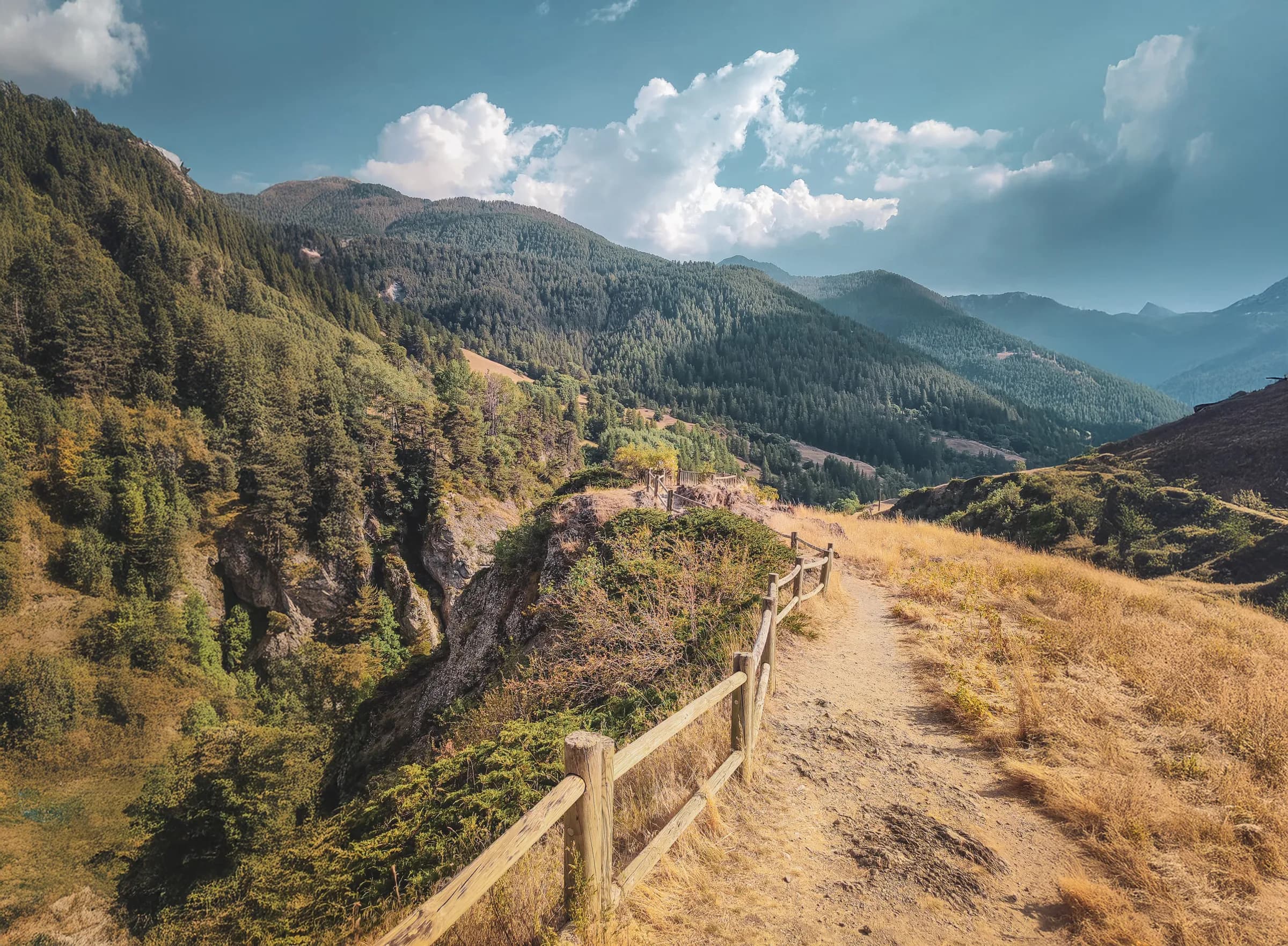 A peaceful trail winding through lush green mountains and bright skies, an invitation to adventure.