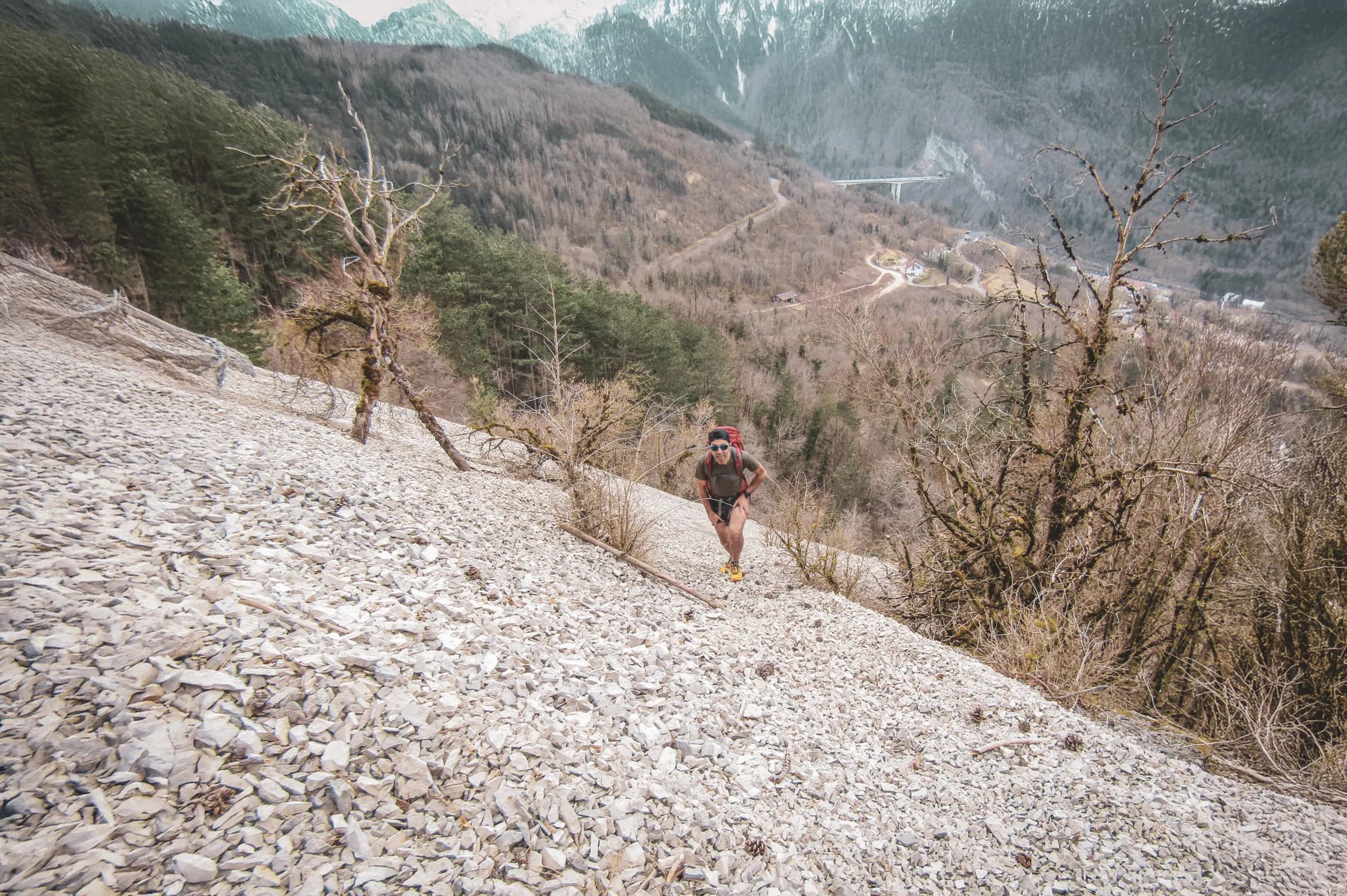 Un coureur en pleine ascension sur un sentier rocheux, entouré de paysages montagneux verdoyants.