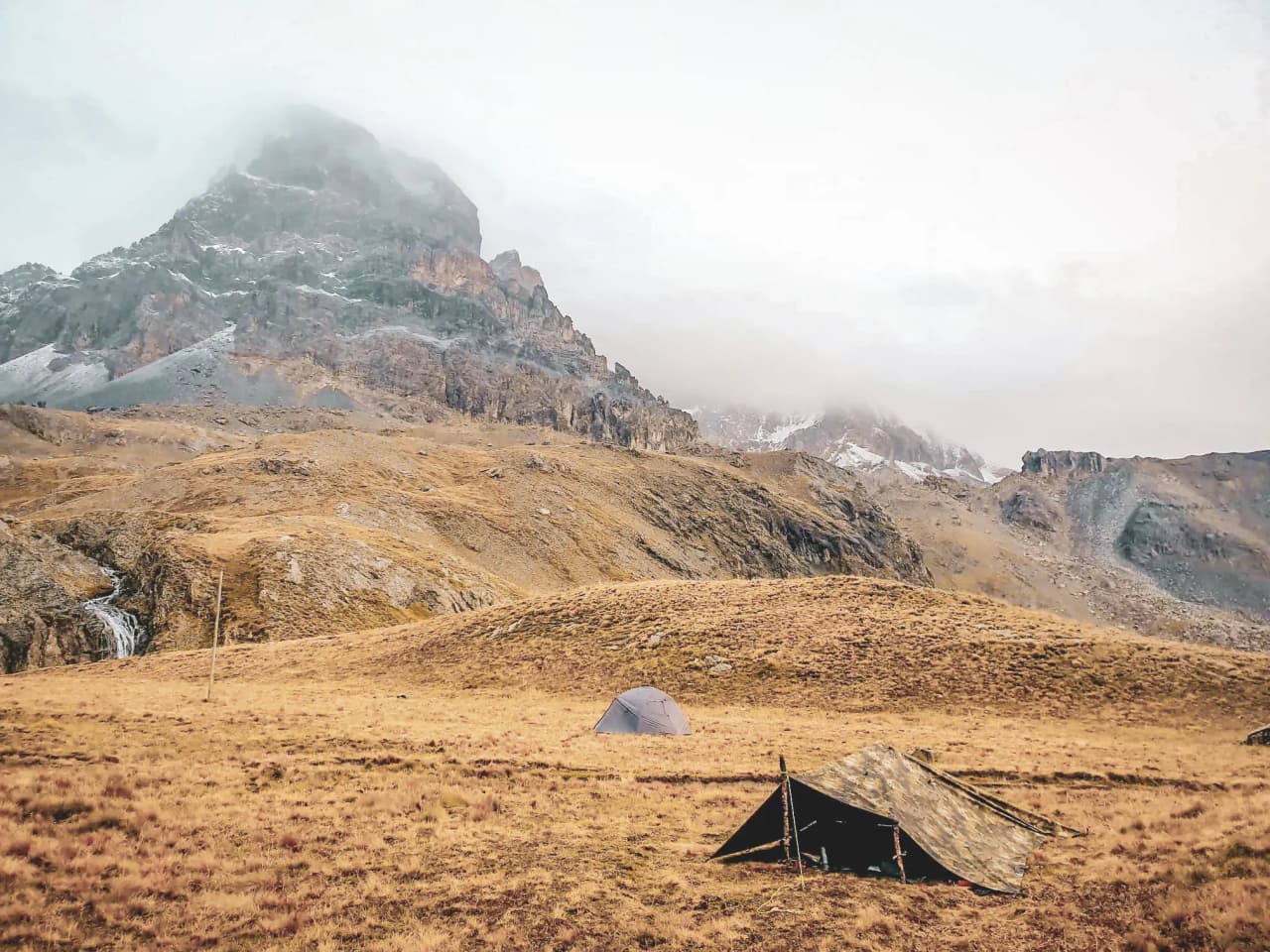 Un paysage alpin majestueux avec des tentes au pied de géants montagneux, invitation à l'aventure.