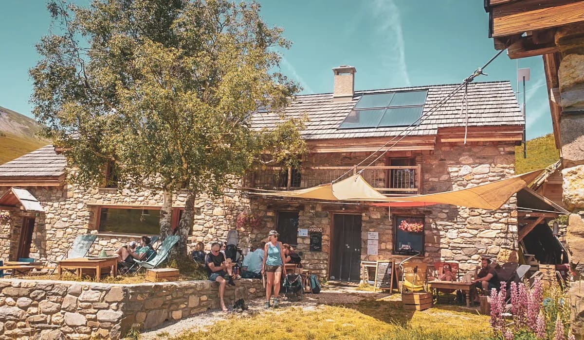 Un chalet en pierre en montagne, entouré de verdure, accueillant des randonneurs en pause.