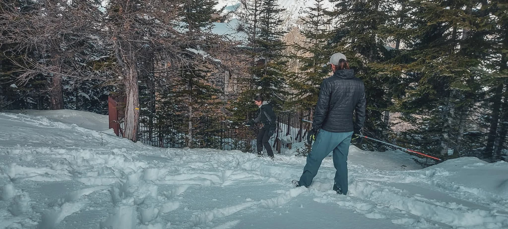 Twee wandelaars in de sneeuw, omringd door bomen, klaar voor een winteravontuur.