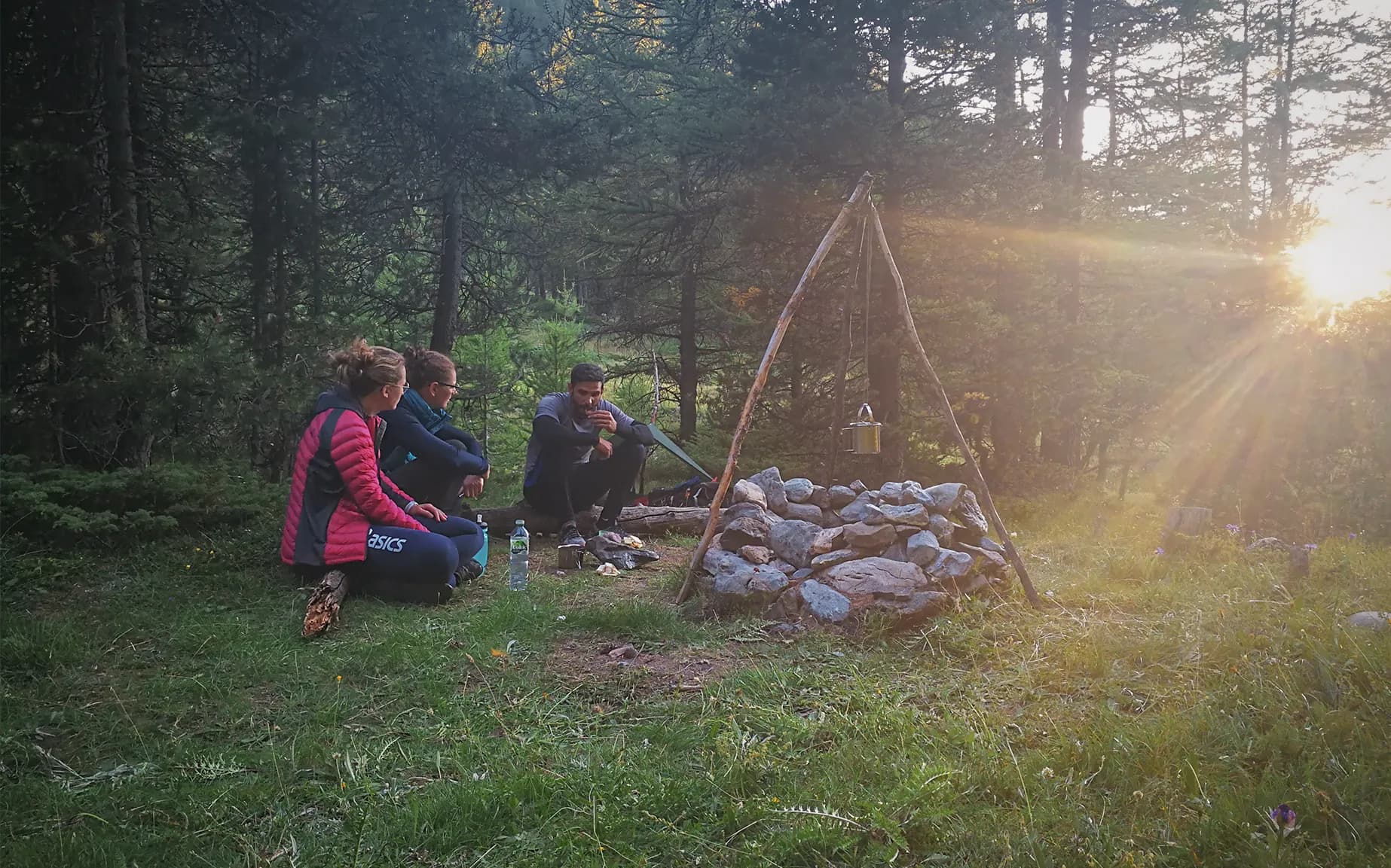 A group in the heart of nature around a campfire, under a golden sun, with an adventurous atmosphere.