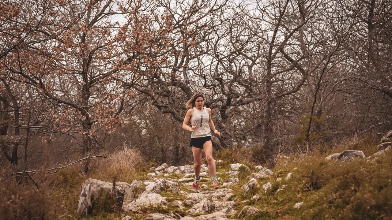 Athlete running on a rocky path surrounded by dry-leaved trees in the Auvergne.