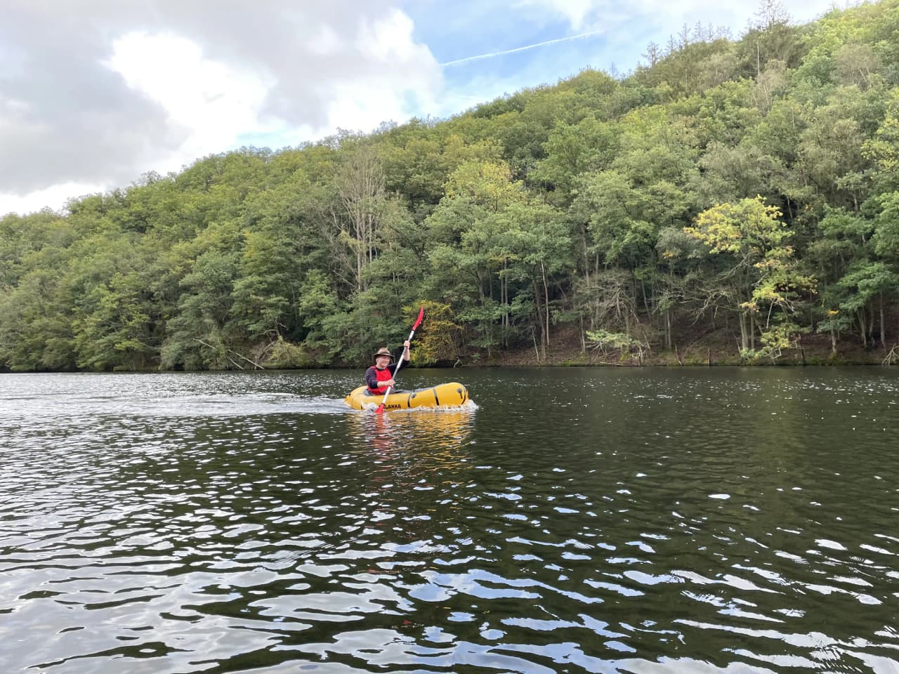 Een avonturier peddelt met een packraft op een rustige rivier, omgeven door weelderig groen.