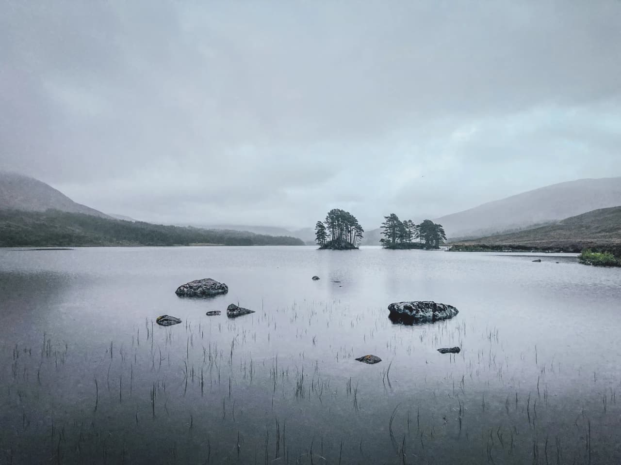 A peaceful lake surrounded by misty hills, an invitation to adventure in the Scottish Highlands.