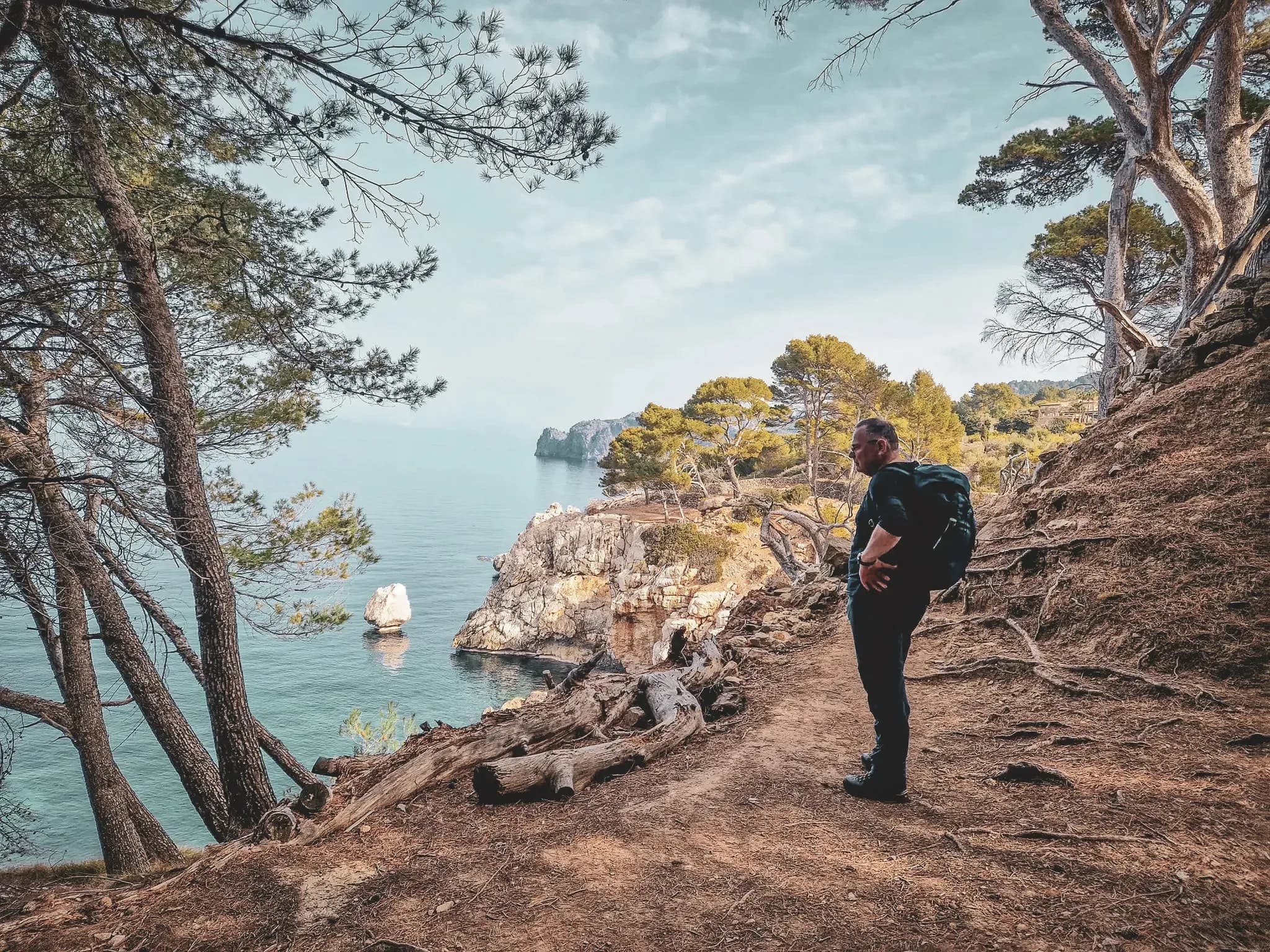 Hiker contemplating the sea in Mallorca, surrounded by pine trees and wild landscapes.