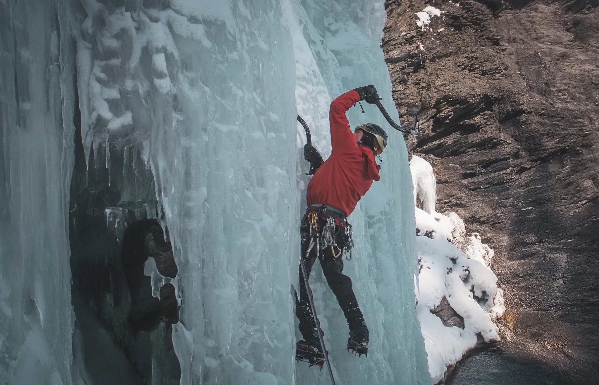 Een klimmer trotseert een glinsterende ijsval in een majestueuze Alpenomgeving.