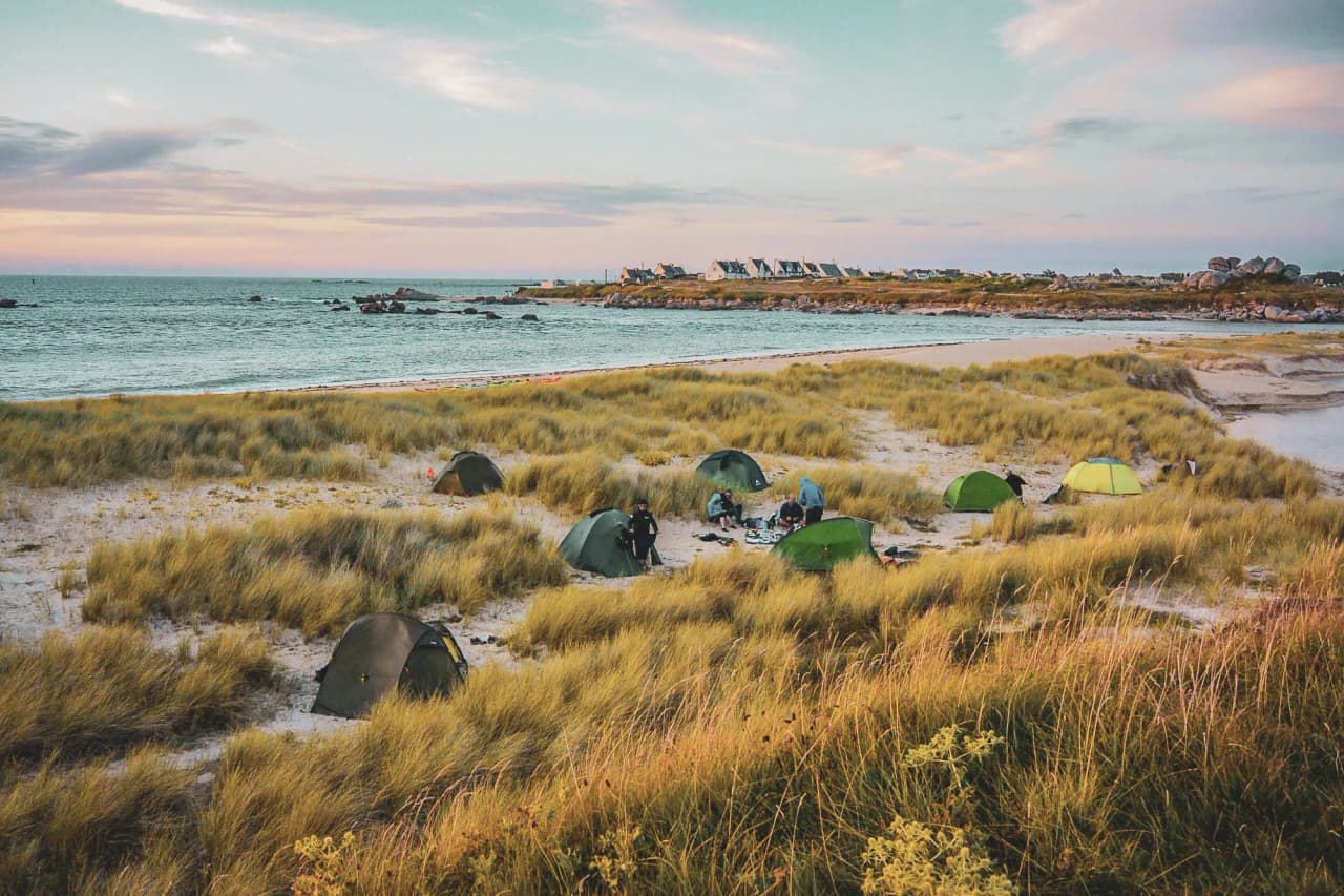 Tents by the sea, surrounded by lush green dunes, for a tranquil adventure.