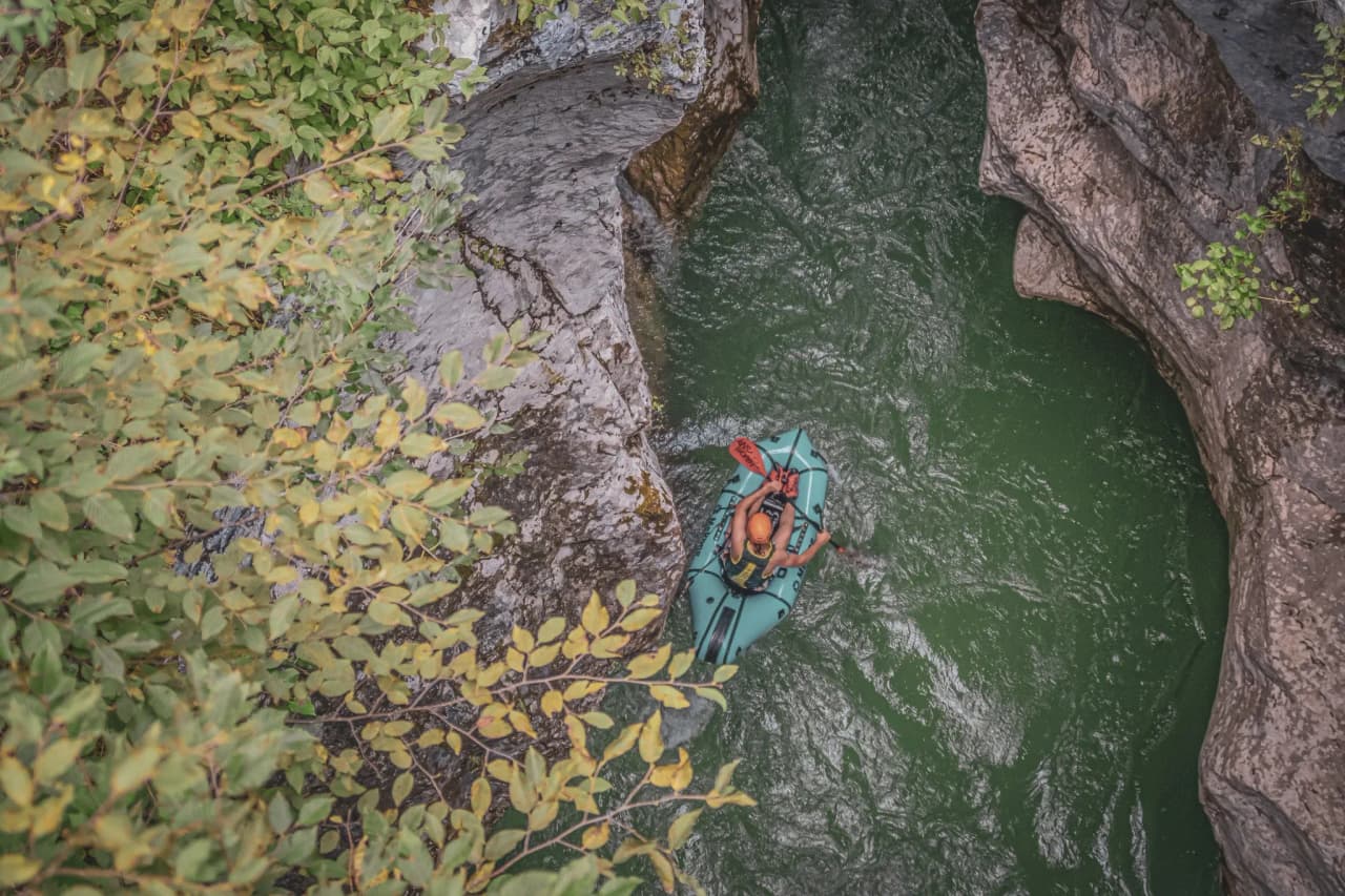 Packraft hiker seen from above in the emerald waters of a canyon, surrounded by sculpted Slovenian cliffs.