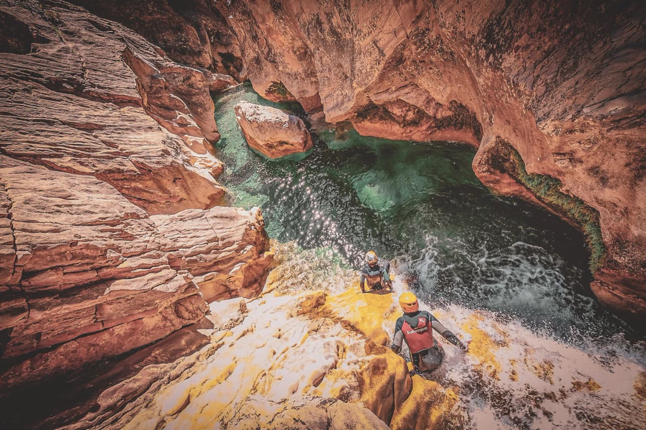 Three canyoning adventurers descend steep cliffs to sparkling turquoise waters.