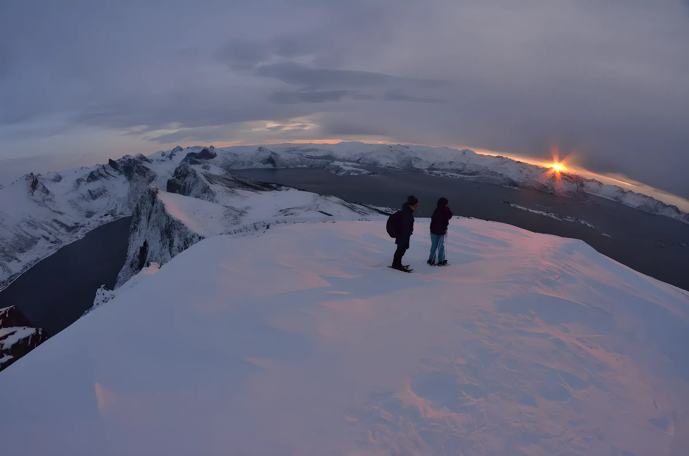 Two hikers watch a spectacular sunset over the snow-covered landscapes of Senja.