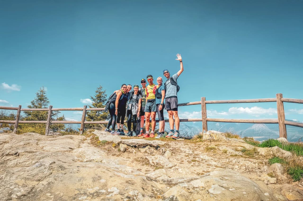 Groupe joyeux de coureurs sur un sommet, entouré de nature et d'un ciel bleu éclatant.