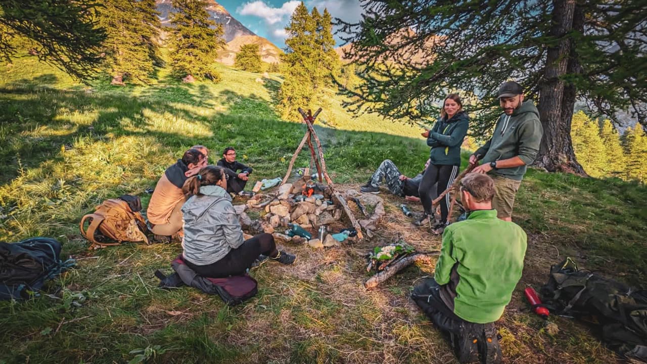 Un groupe de personnes se rassemble autour d'un feu de camp dans la vallée verdoyante de l'Ubaye.