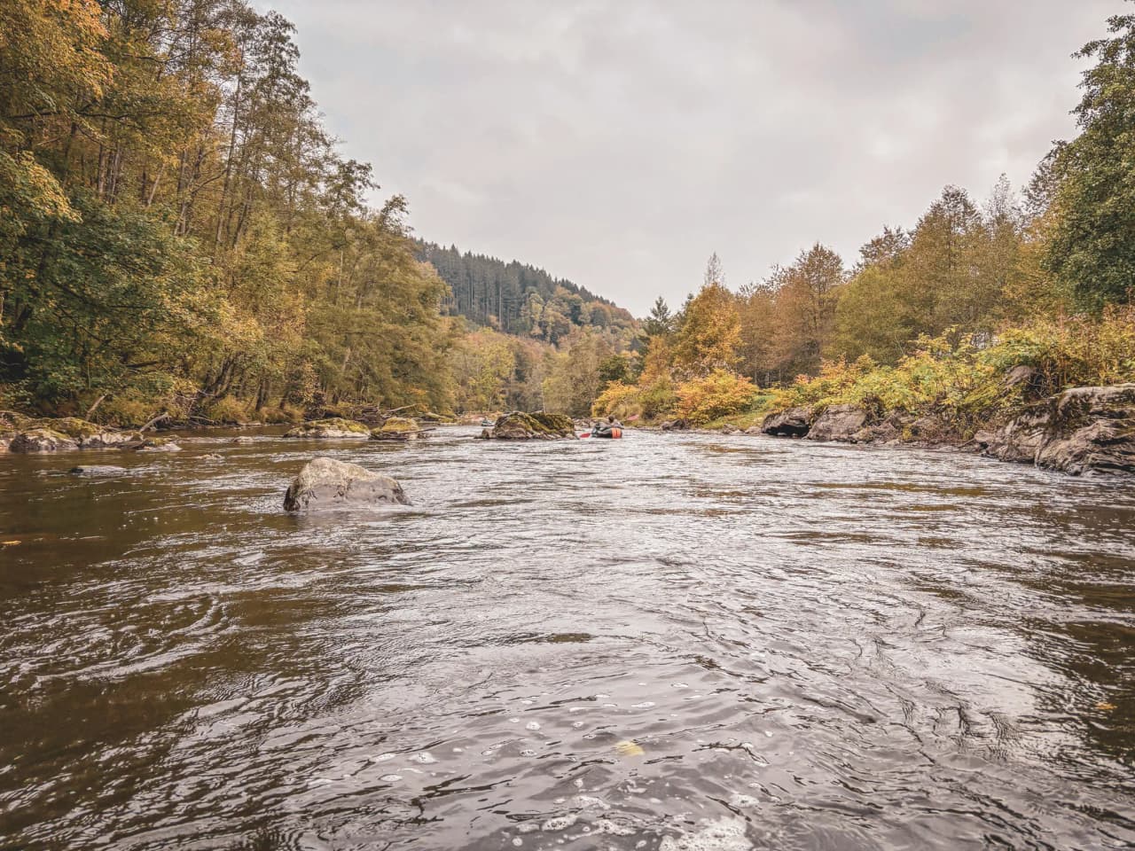 A tranquil river in the Ardennes, surrounded by colourful forests and rocky outcrops, ideal for adventure.