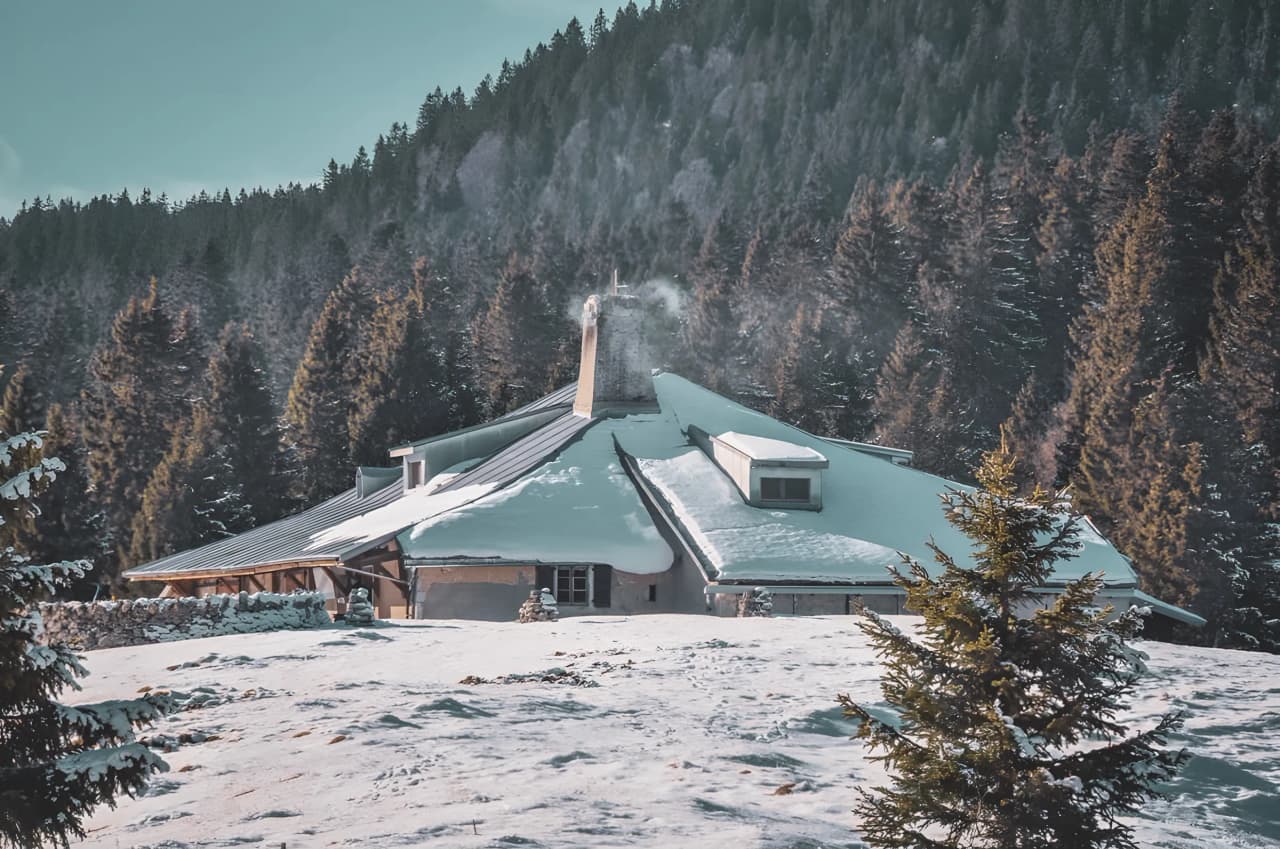 Un chalet enneigé, entouré de forêts, offre une évasion hivernale au cœur du Jura suisse.