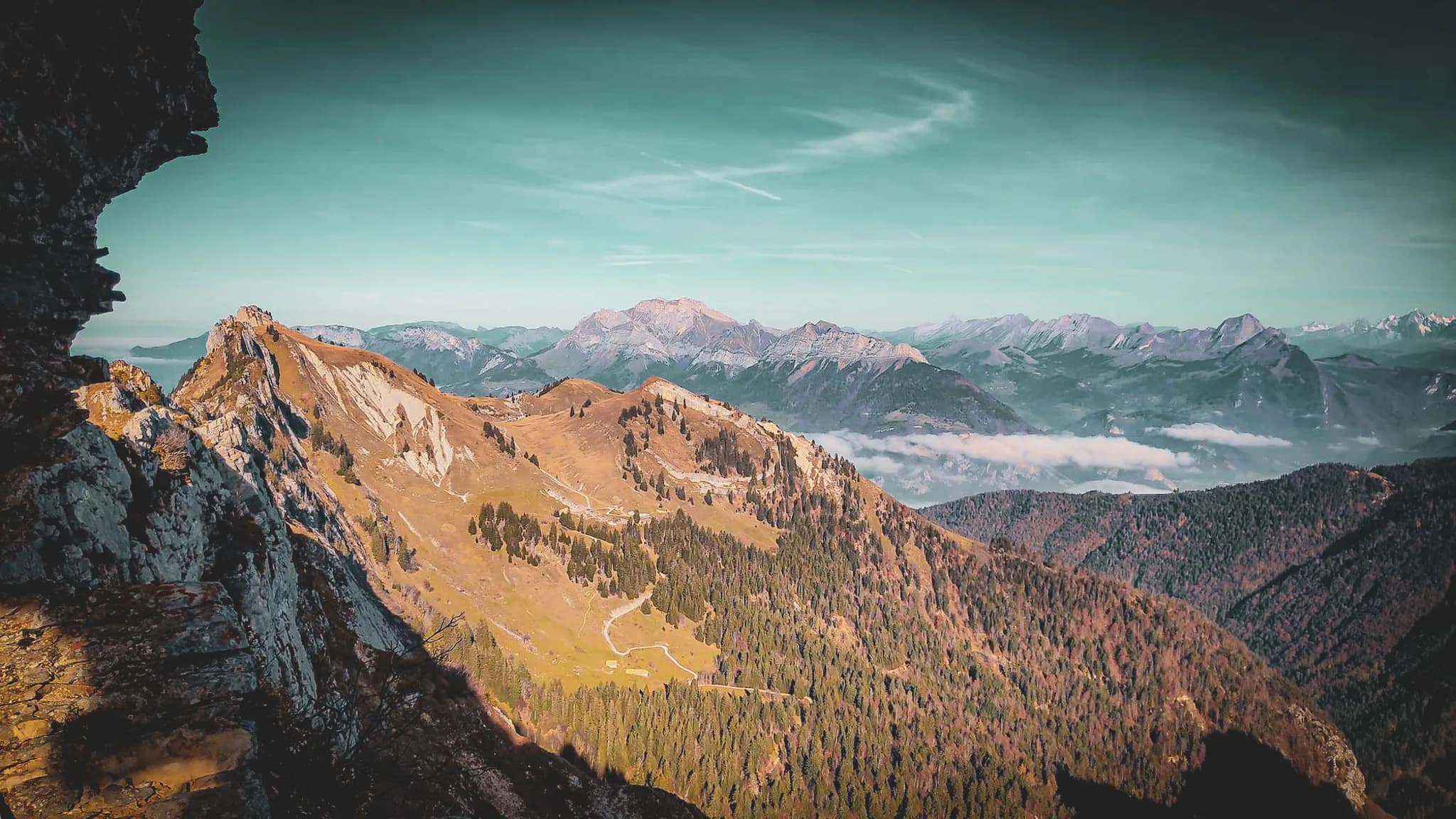 Un paysage montagneux spectaculaire, avec des sommets majestueux et des vallées verdoyantes. À l'avant, un sol escarpé, parsemé de conifères, se prolonge vers des pentes douces. À